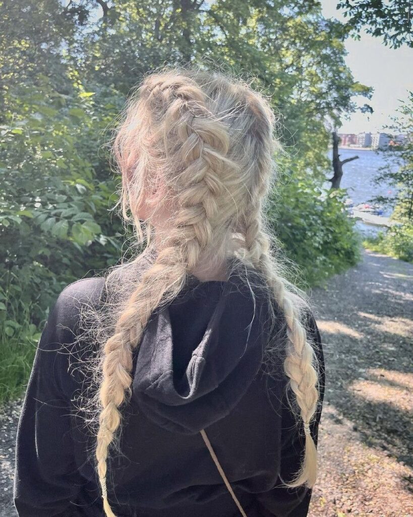 Blonde hair styled in two loose, wavy braids from a back view outdoors.