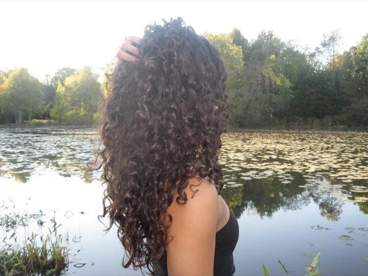 Woman with long, dark brown spiral curls standing before a calm pond.