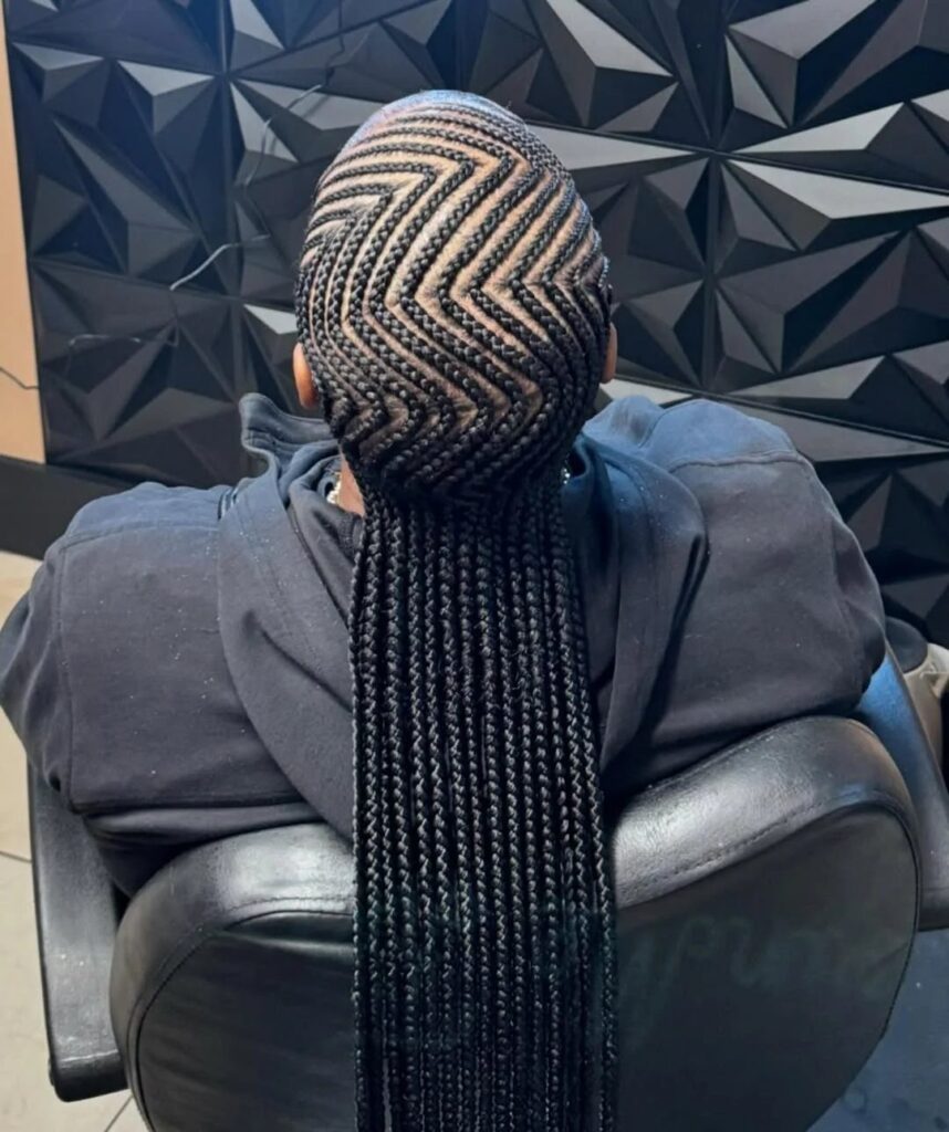 Zig-zag cornrow hairstyle on a person with long black braids from behind.