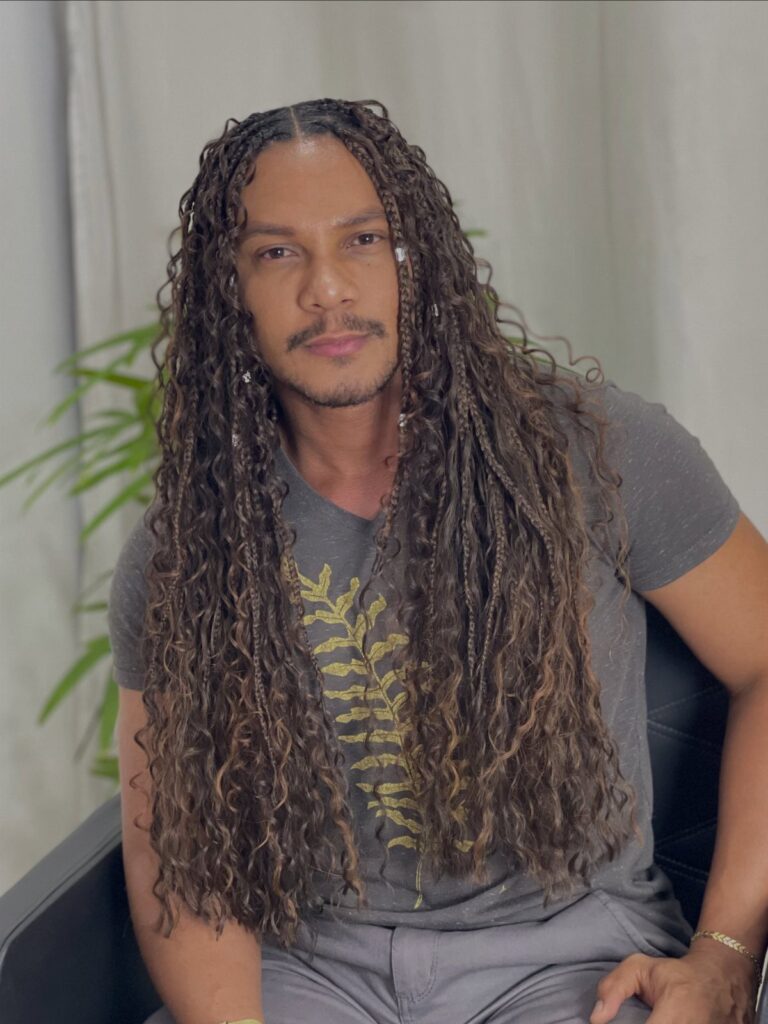 Man with long brown braided hair and curly ends wearing a grey t-shirt.