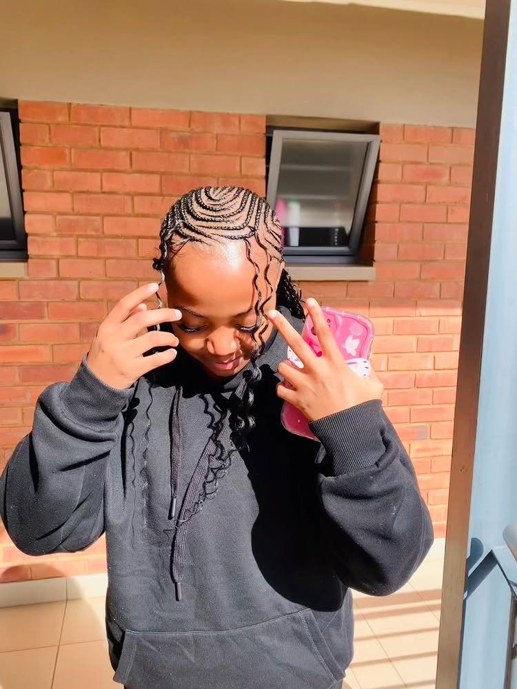 Person with cornrows going back and long curly extensions wearing a black hoodie.