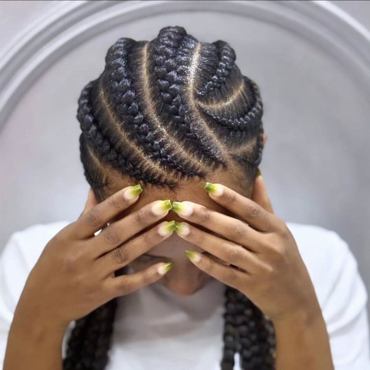 Person with curved cornrows hairstyle covering their face with manicured hands.