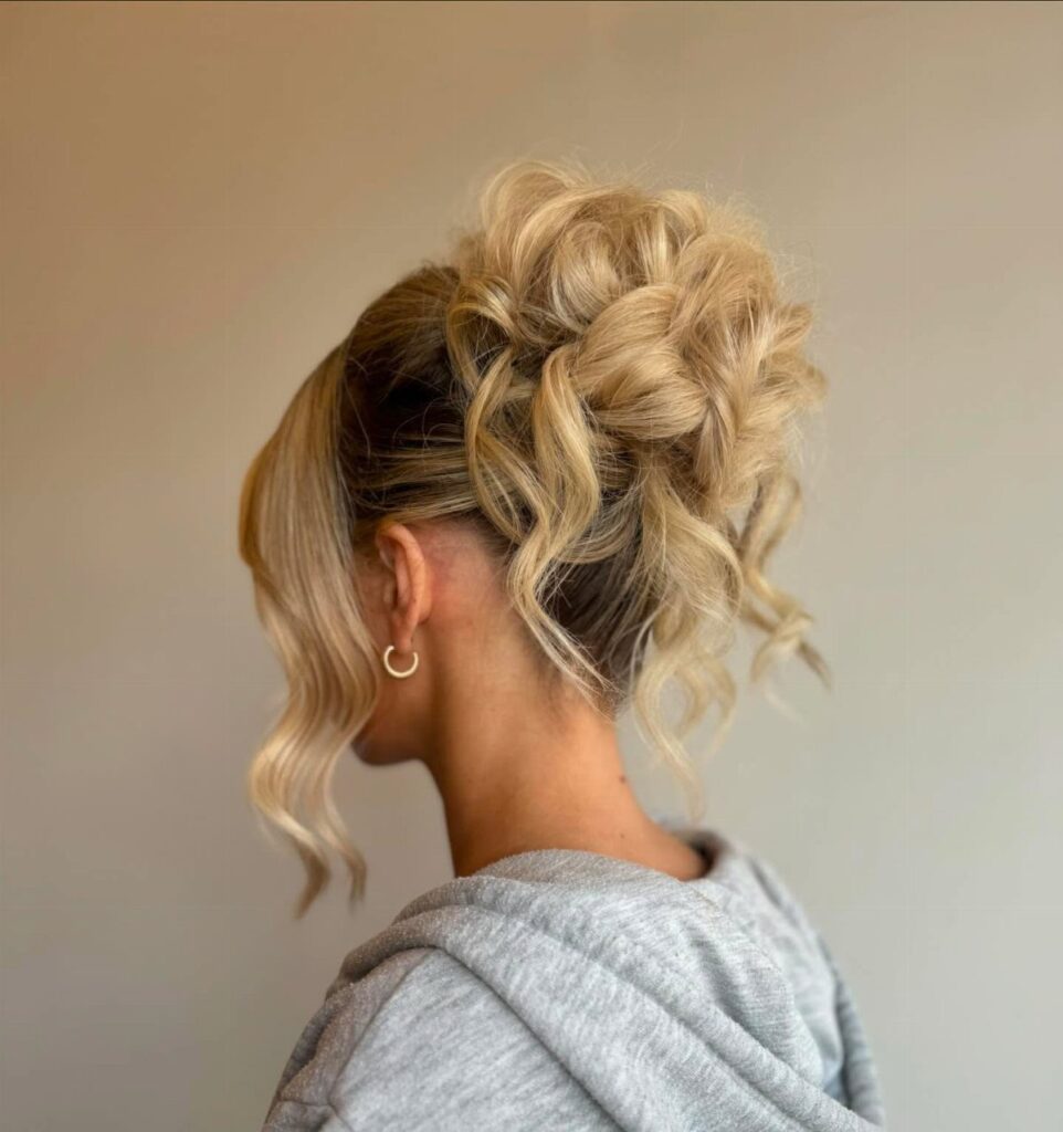 Blonde hair styled in a high curly bun with loose face-framing tendrils.