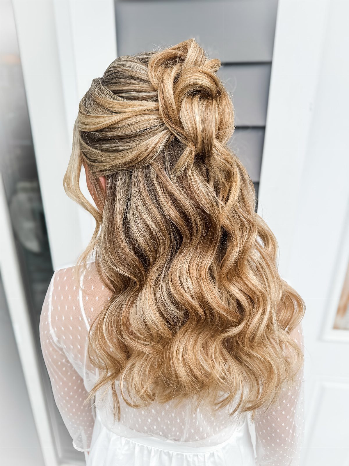 Blonde wavy hair styled in a half-up twisted knot half-updo from behind.