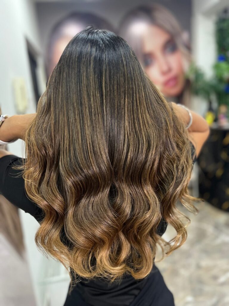 Woman with long wavy dark brown hair and golden blonde highlights from behind