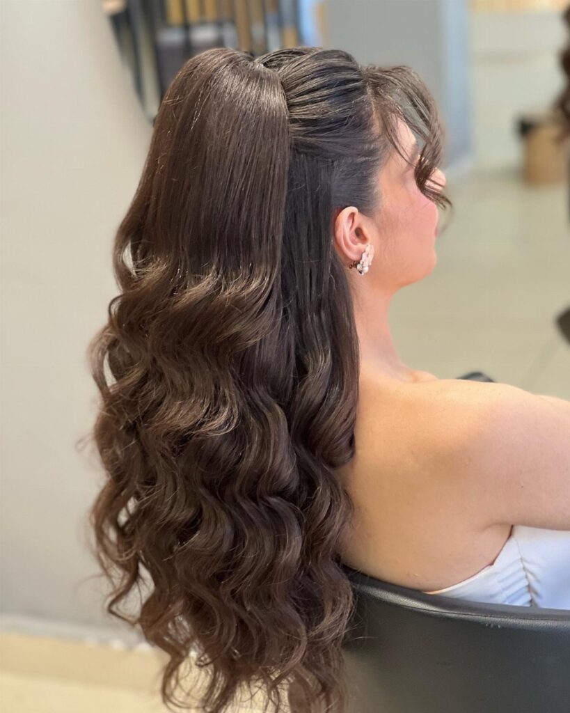 Woman with long brown wavy hair in an elegant half-up, half-down hairstyle.