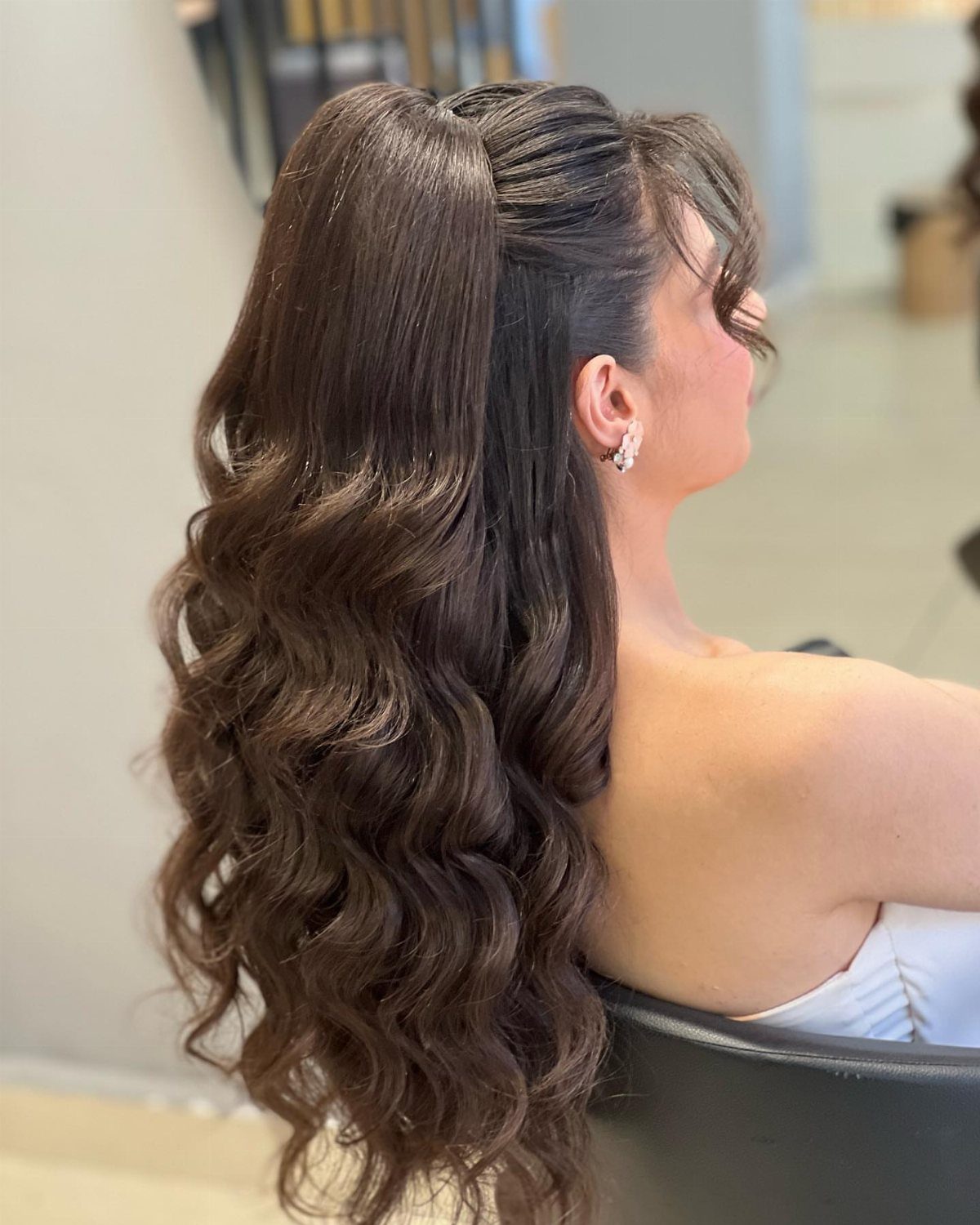 Woman with long brown wavy hair in an elegant half-up, half-down hairstyle.