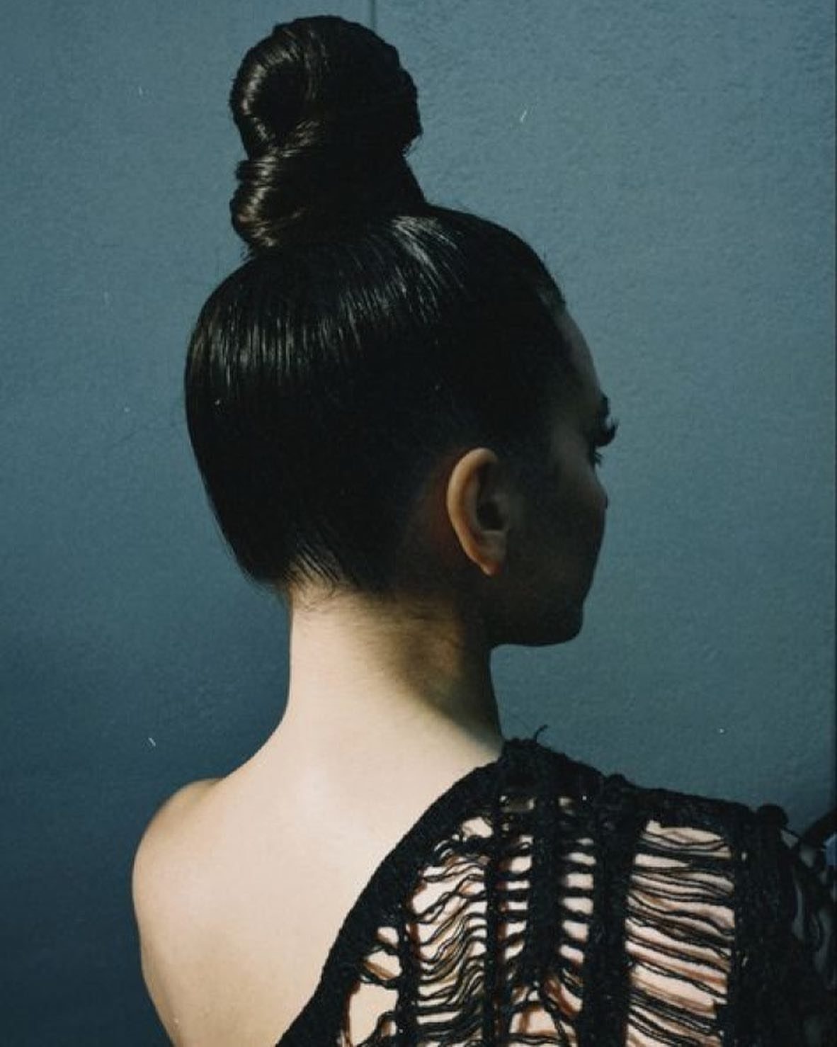 Woman with dark hair styled in a sleek, high top knot bun.