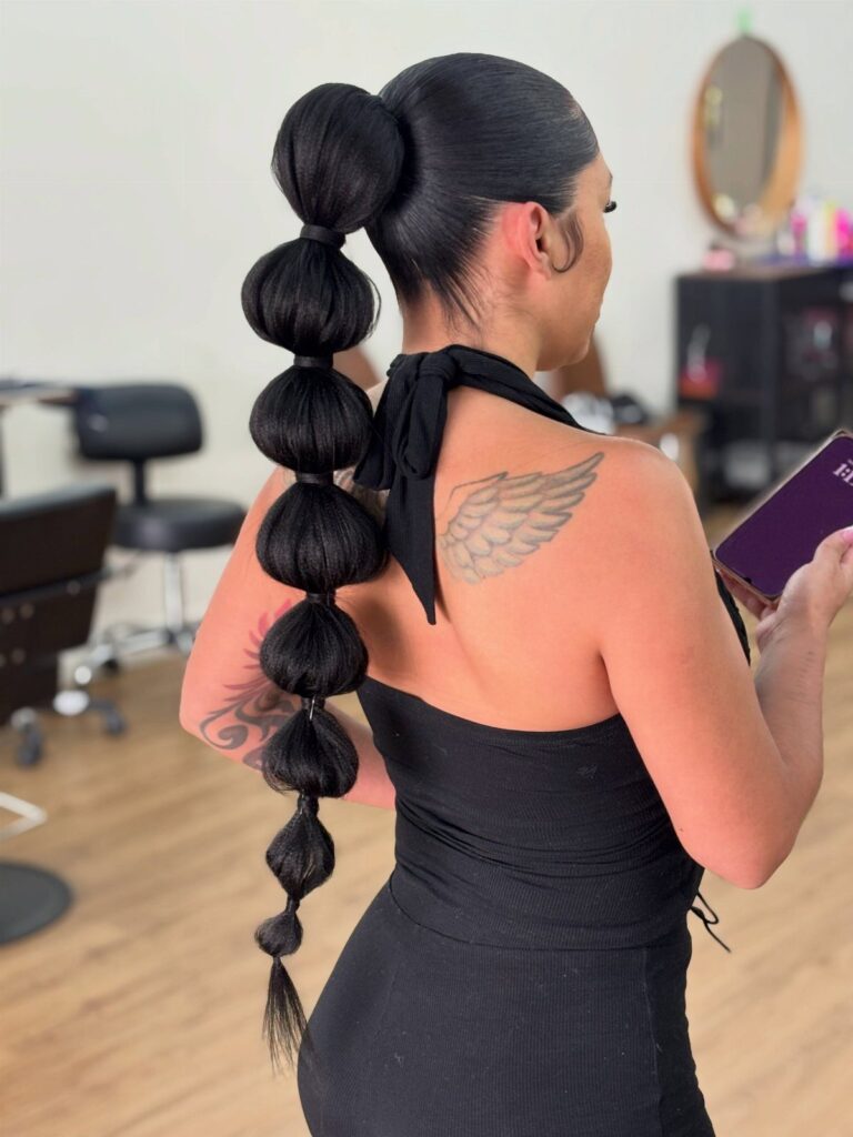 Woman with a high bubble ponytail hairstyle and a wing tattoo on her shoulder.