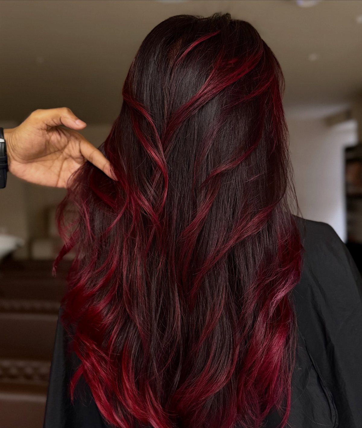 Long wavy dark hair with blended burgundy balayage highlights seen from behind.