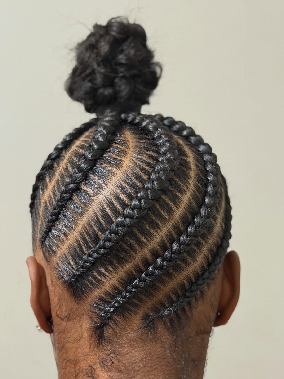 Cornrow braids on a person's head leading into a small top bun.