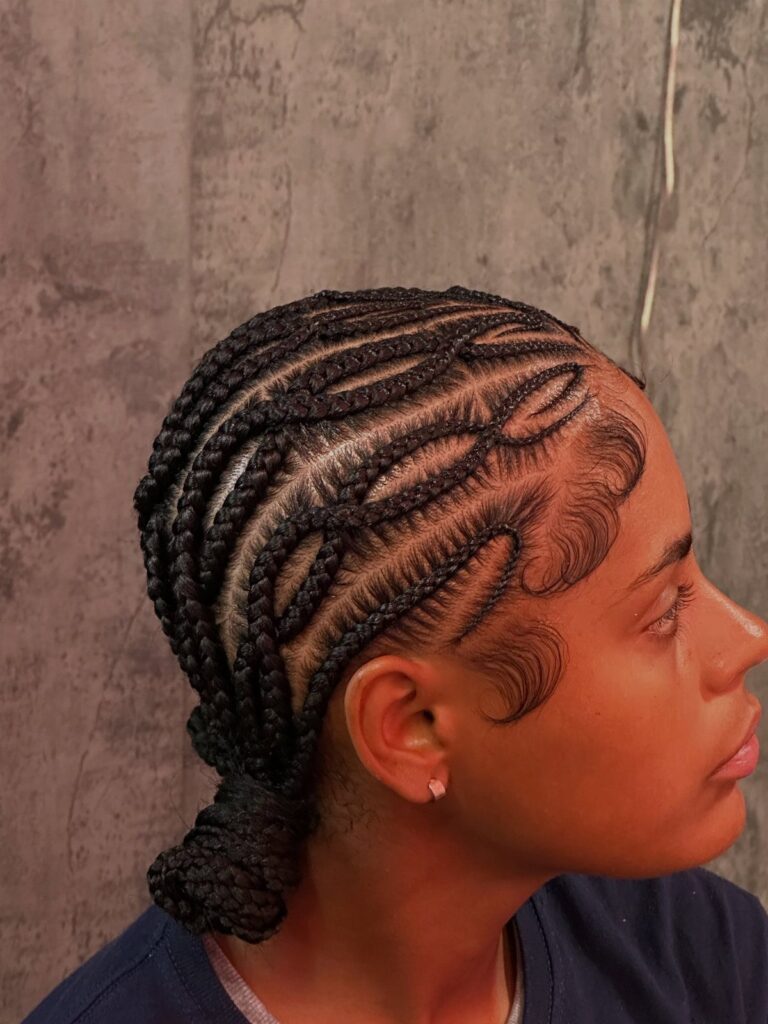 Woman with black hair styled in curved feed-in cornrow braids and a bun.