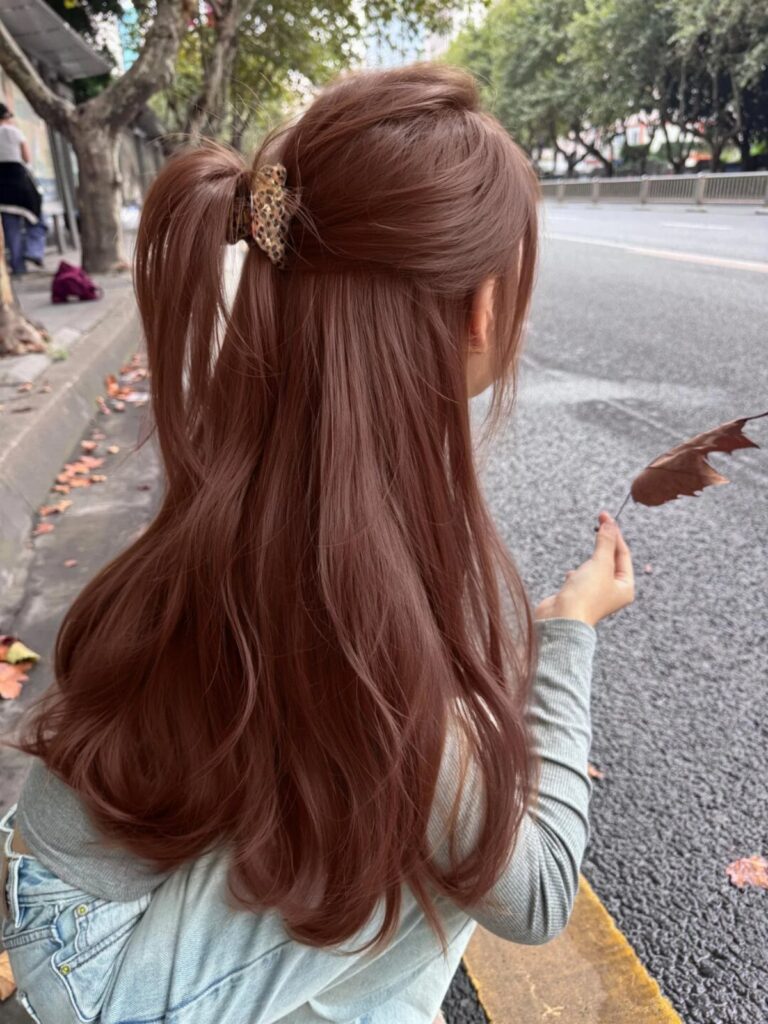 Woman with long wavy reddish-brown hair tied in a half-up ponytail outdoors