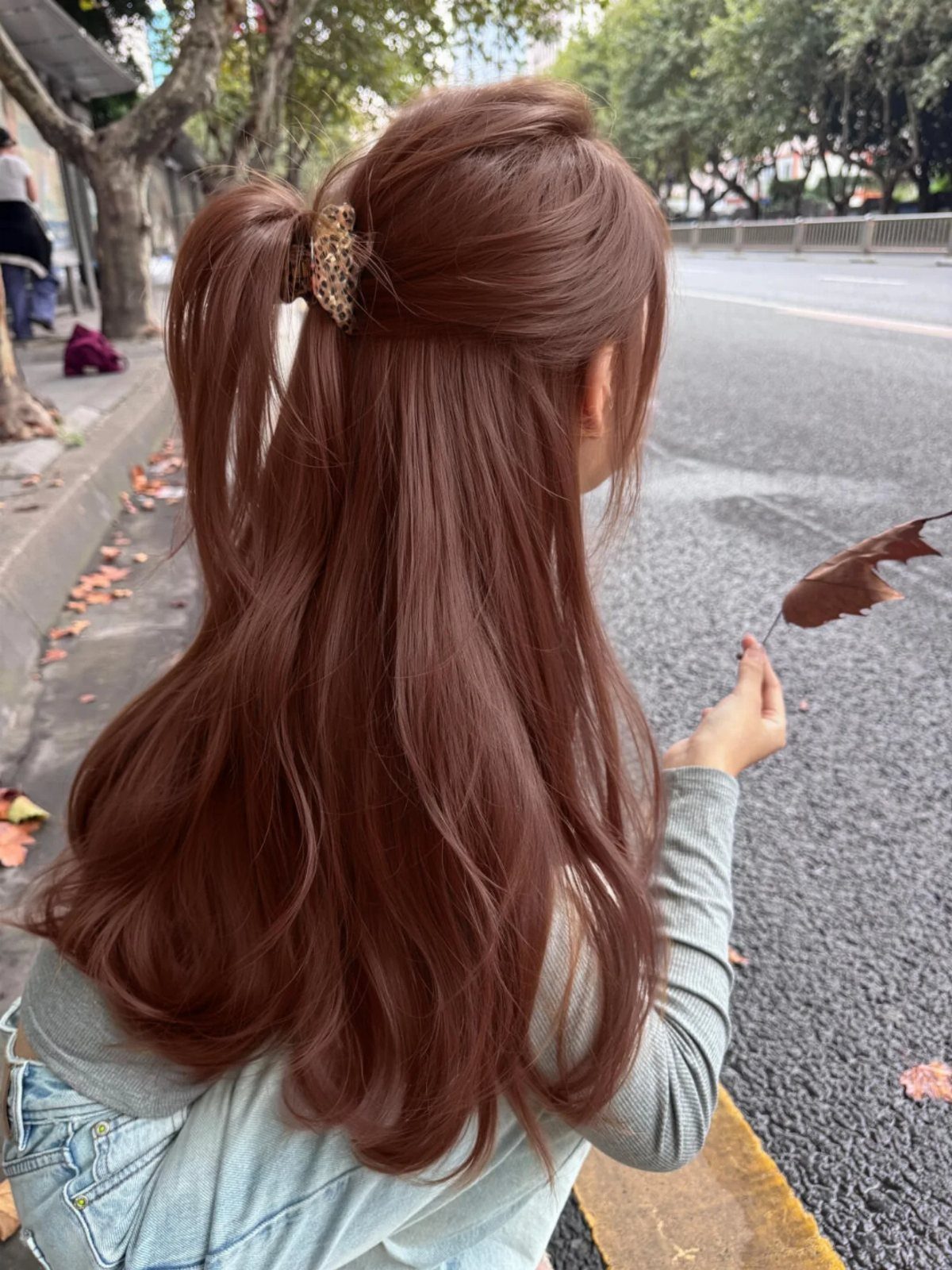 Woman with long wavy reddish-brown hair tied in a half-up ponytail outdoors