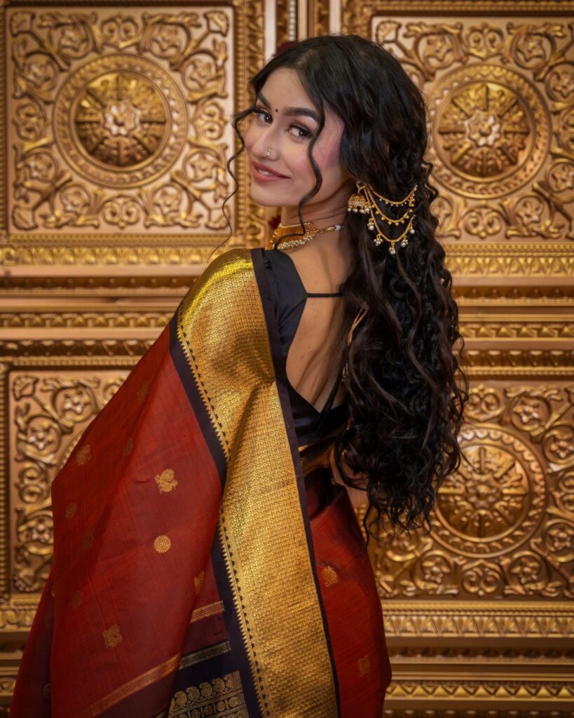 Woman in red saree with long side-swept curls and gold jewelry
