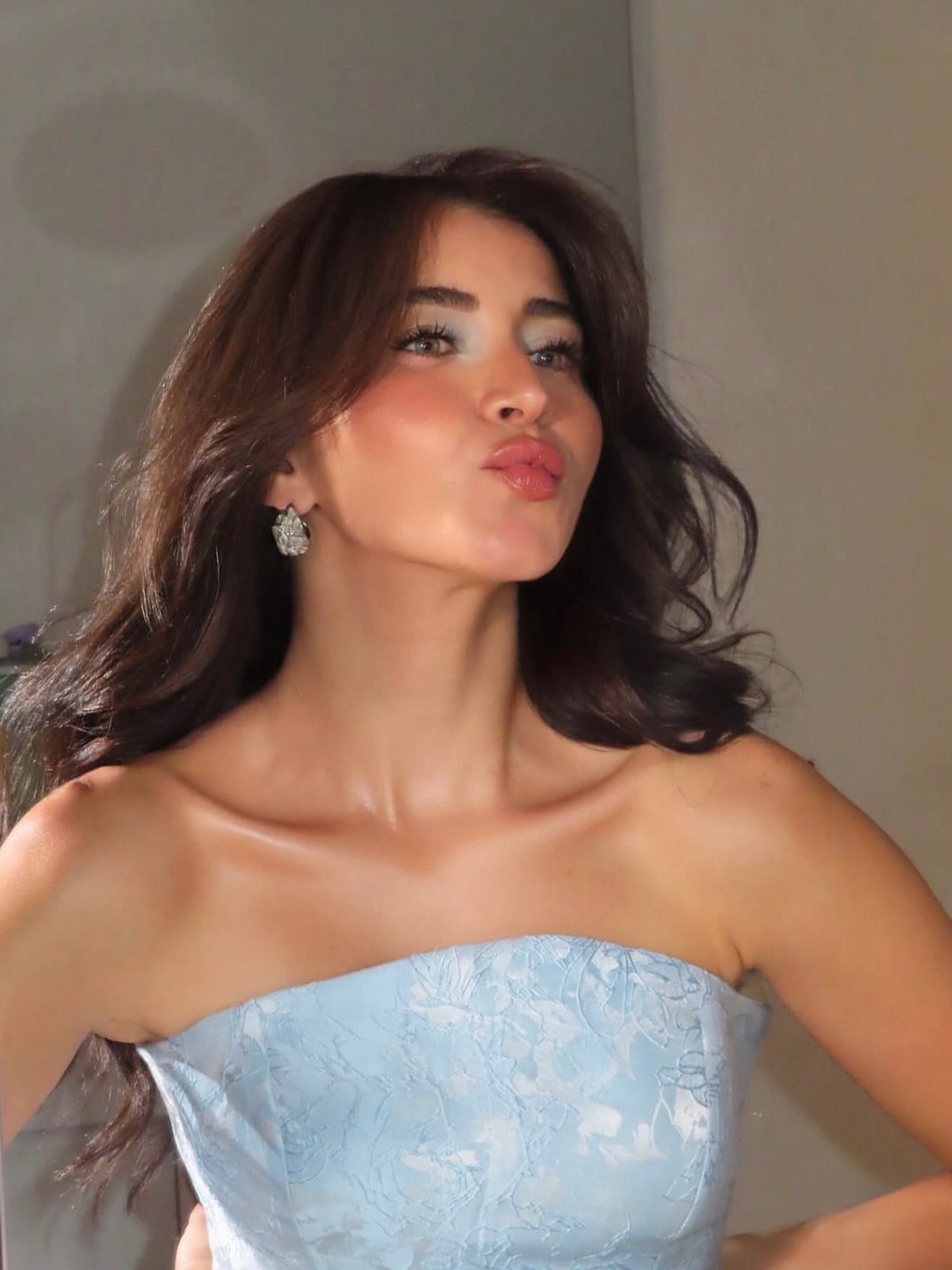 Woman with voluminous brown bouncy blowdry hair wearing a light blue strapless dress.