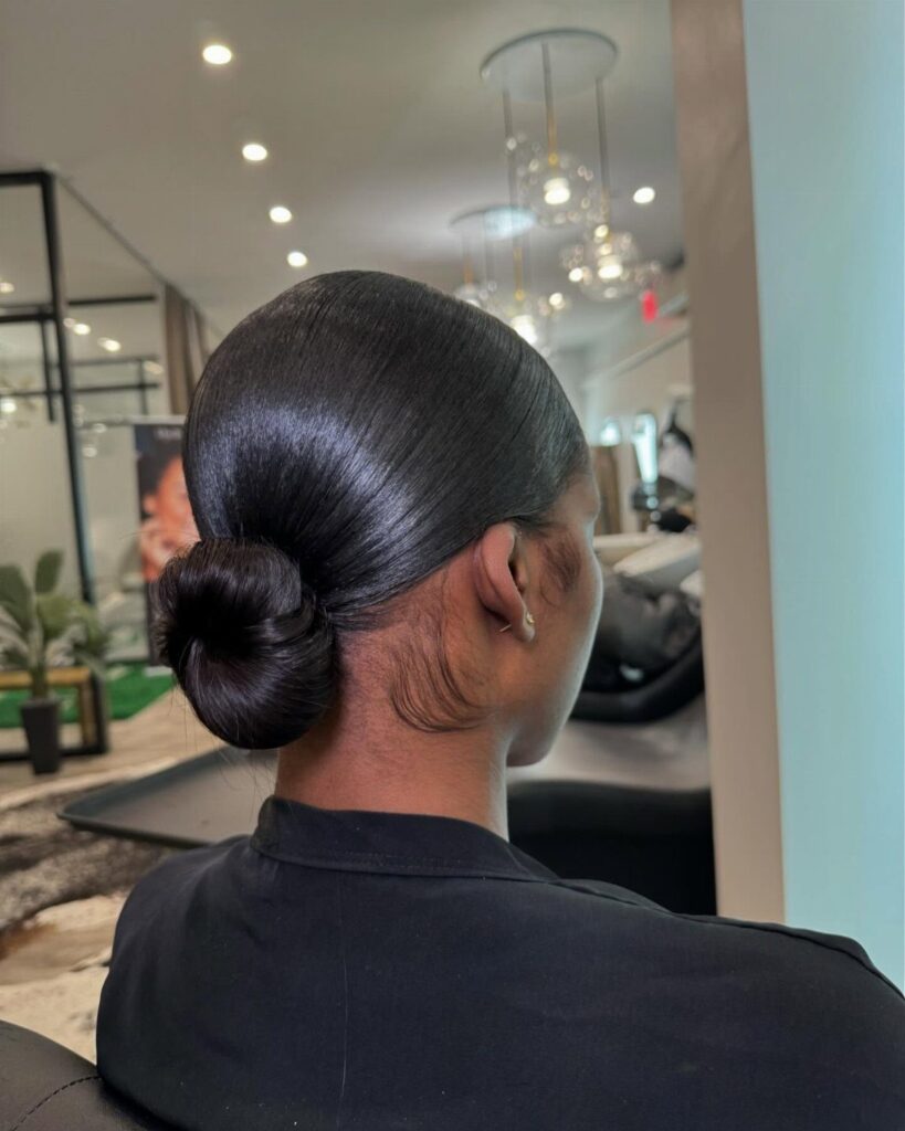 Woman with sleek dark hair styled into a smooth, tight low bun.
