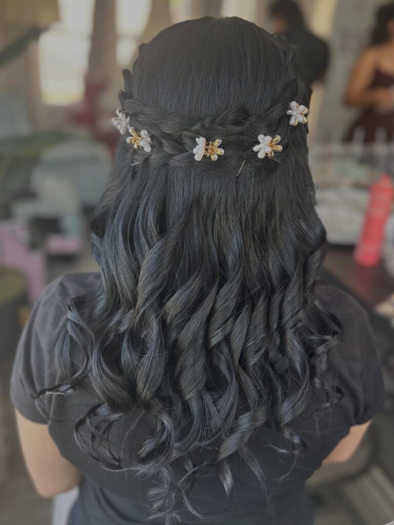 Dark curly hair styled in a braided crown with small floral hair accessories.