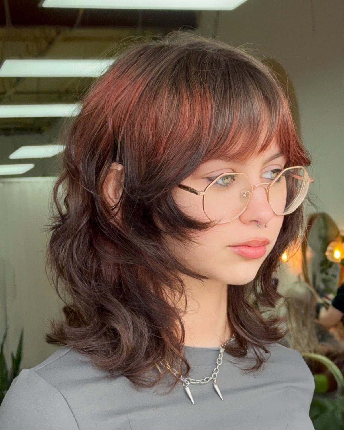 Woman with layered shoulder-length shag curly hair and bangs wearing gold glasses.