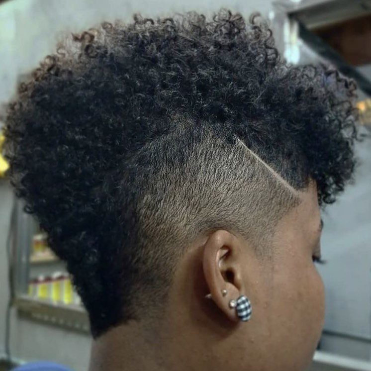Person with a curly mohawk hairstyle featuring shaved sides and a carved line design.