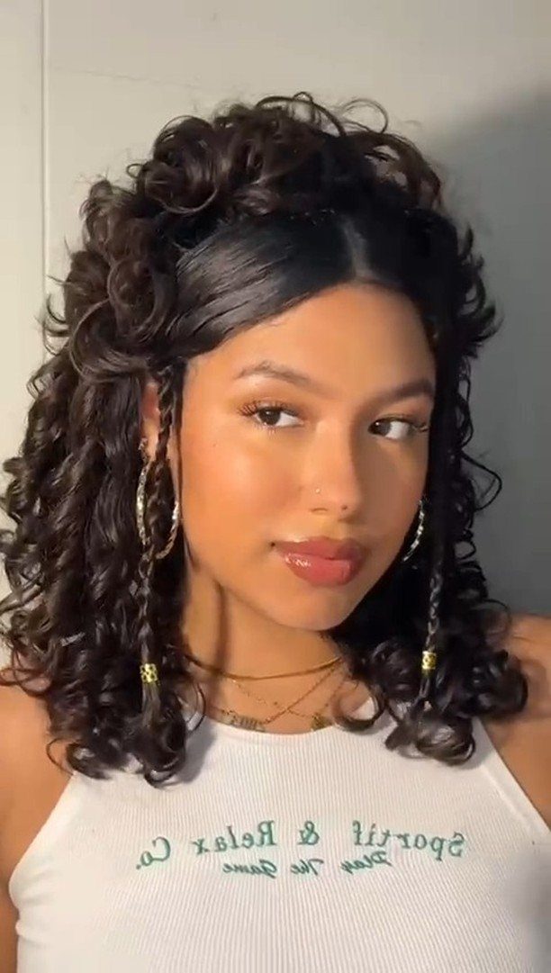 Young woman with curly dark hair in a half-up, half-down hairstyle and gold jewelry.