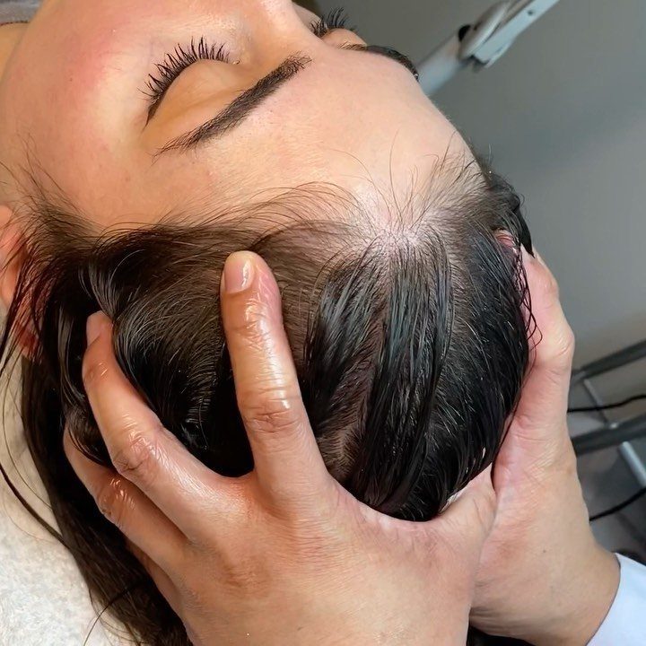 Hands massaging the scalp of a person with wet dark hair and closed eyes.