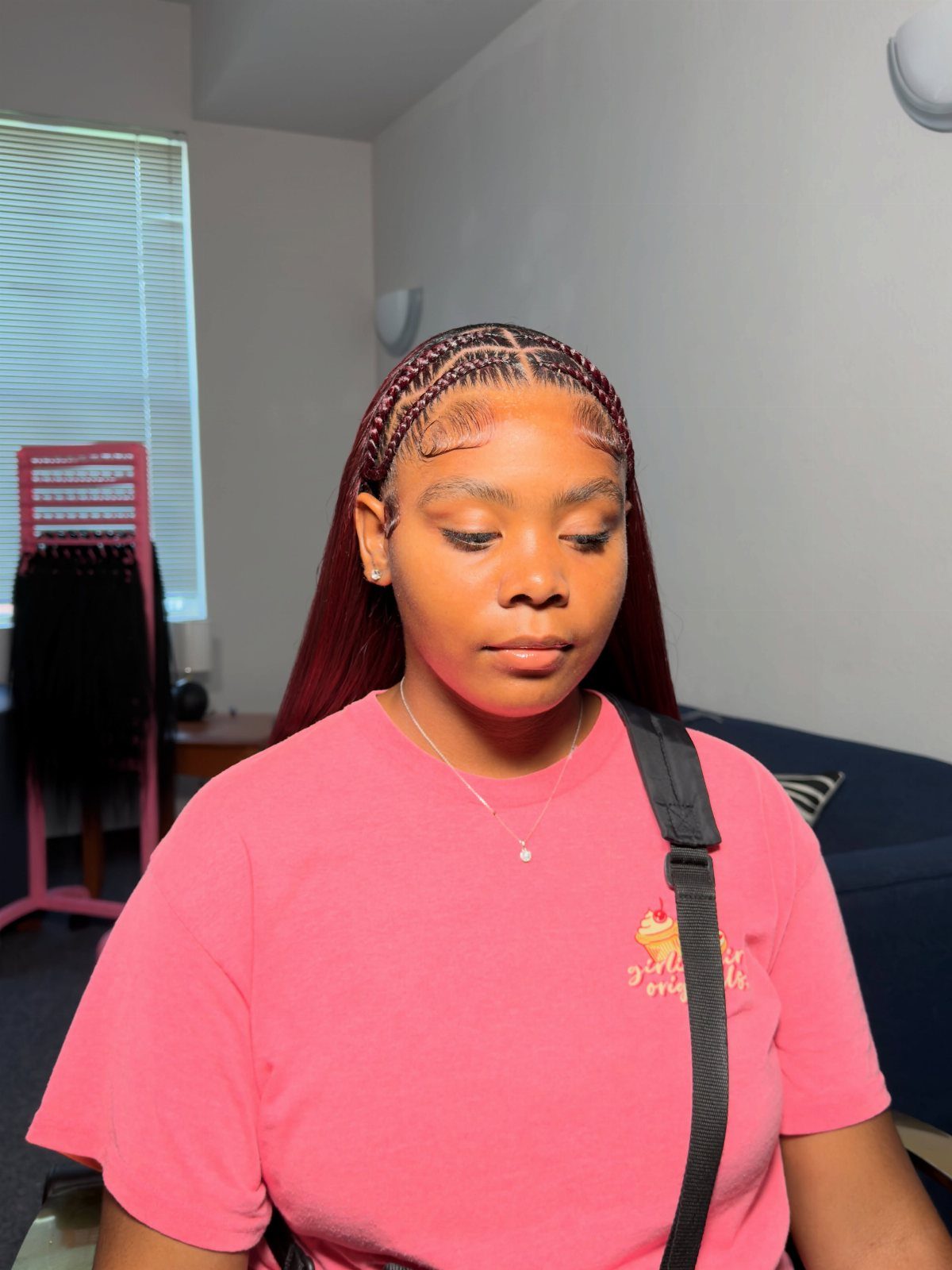 Woman with burgundy hair featuring small braids along the crown and a pink shirt.