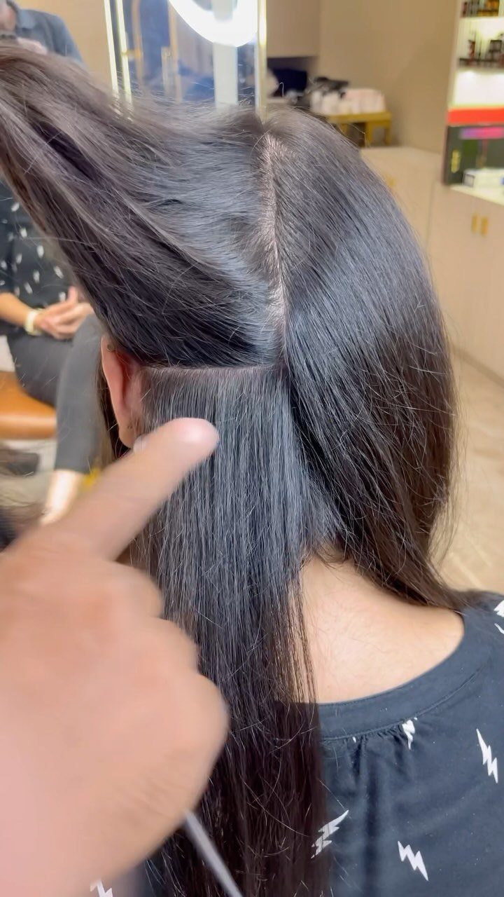 Dark hair being sectioned horizontally by a hand in a salon setting.