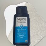 Nizoral Anti-Dandruff Shampoo bottle on a white textured organic shaped background