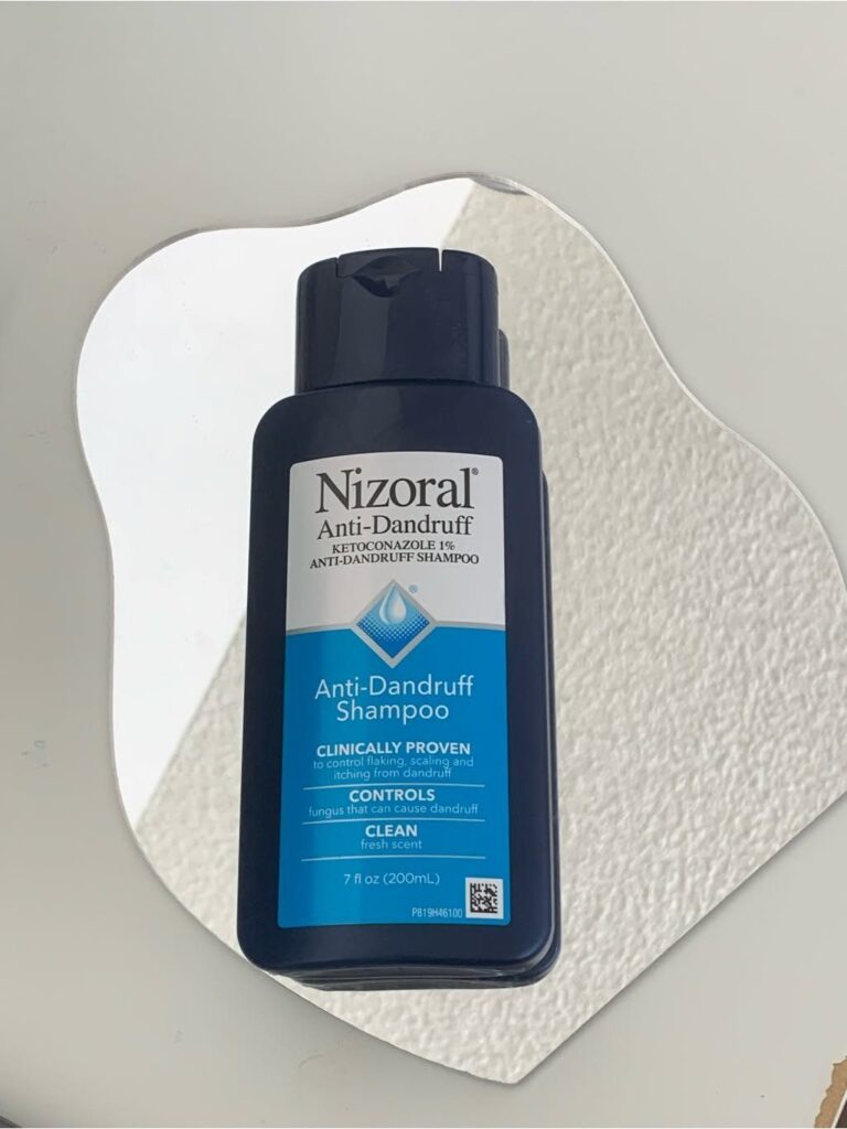 Nizoral Anti-Dandruff Shampoo bottle on a white textured organic shaped background