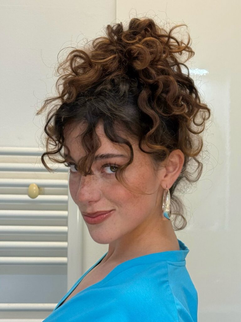 Woman with brown curly hair styled in a high updo and face-framing curls.