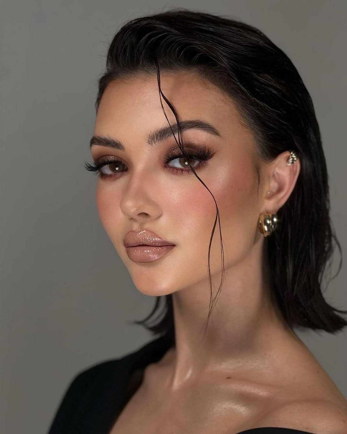 Woman with dark slicked-back wet look hair and glowing makeup against grey background