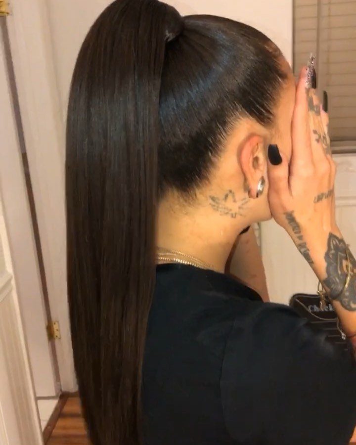 Woman with a sleek high ponytail and tattoos on her neck and hand.