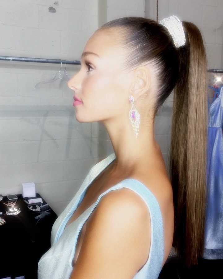 Woman with a slicked-back high ponytail and white scrunchie in profile view.
