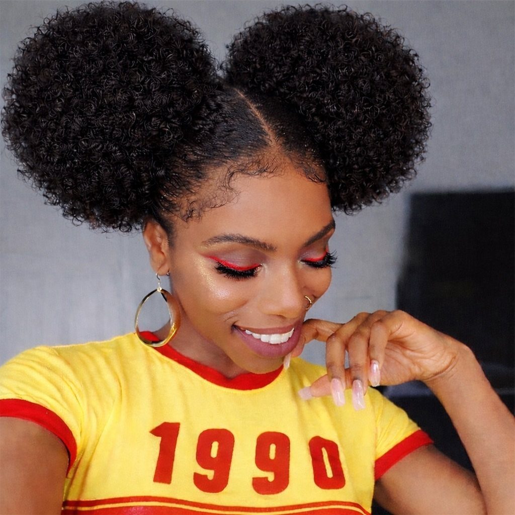 Woman with two large curly hair puffs wearing a yellow 1990 t-shirt.