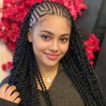 Woman with long black twisted braids and geometric scalp parting patterns.